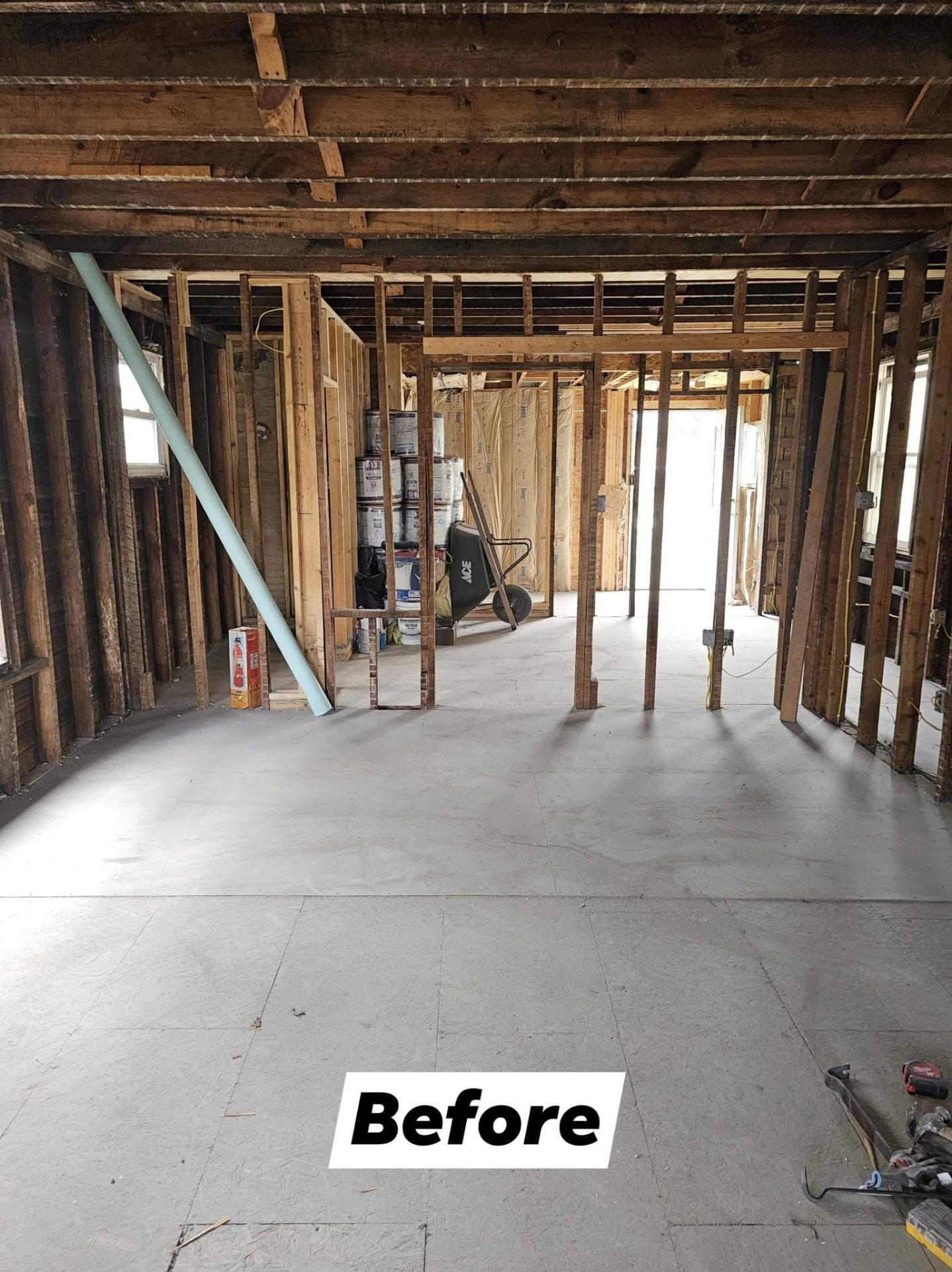Open room stripped to the studs with exposed framing and subfloor before renovation